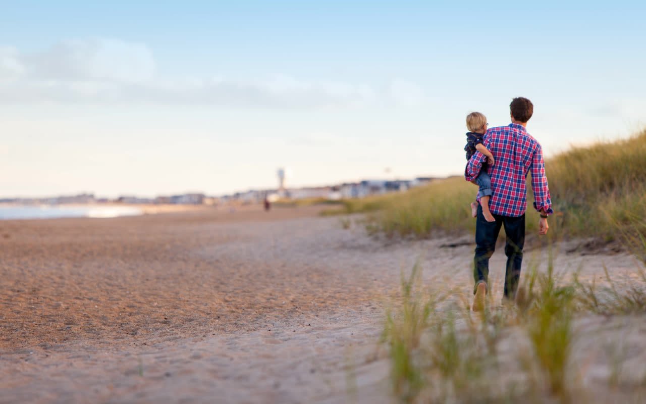 A father carrying his young child along a beach path