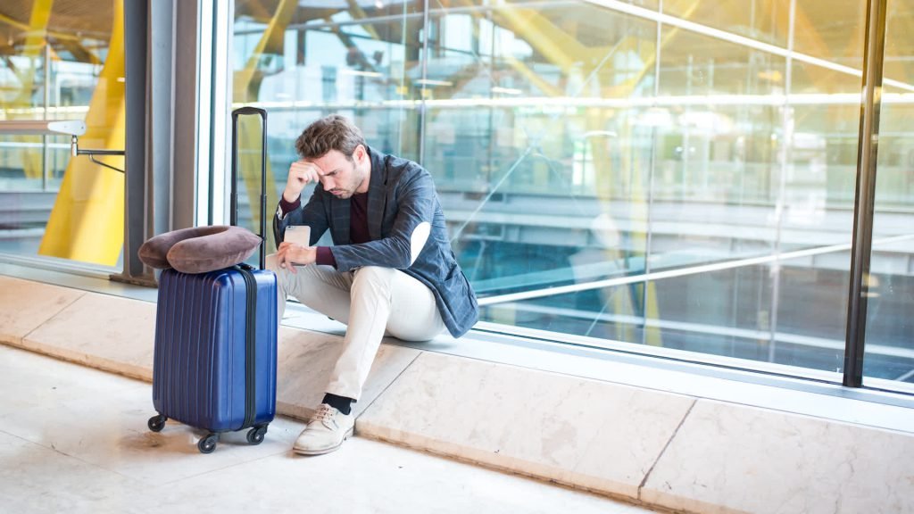 A worried traveller sitting with his luggage at an airport